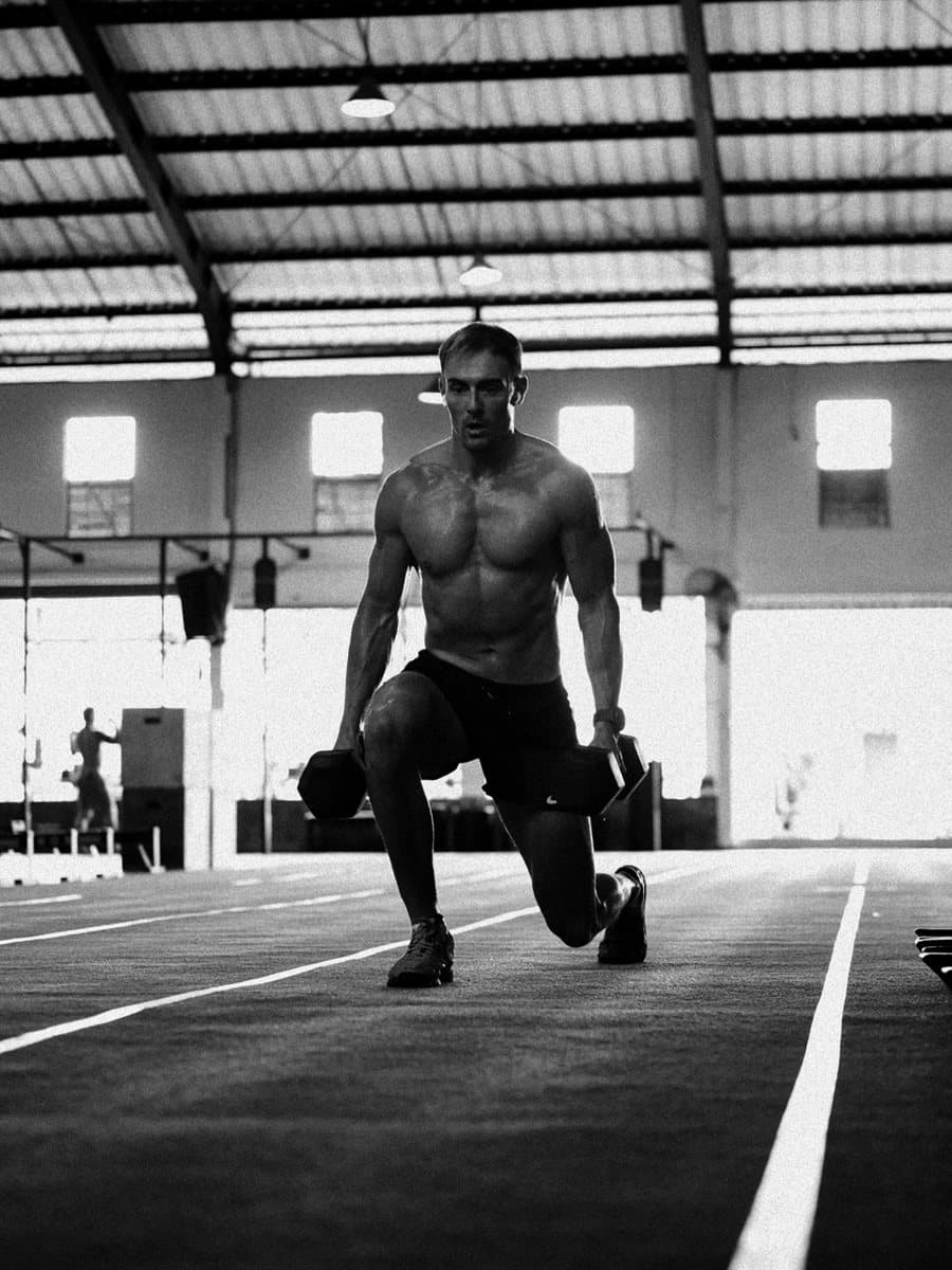 James mid-lunge with dumbbells on the gym turf